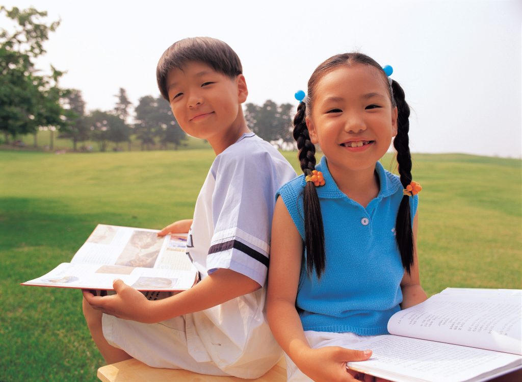 A boy and a girl reading children's literature books and smiling while sitting outside.