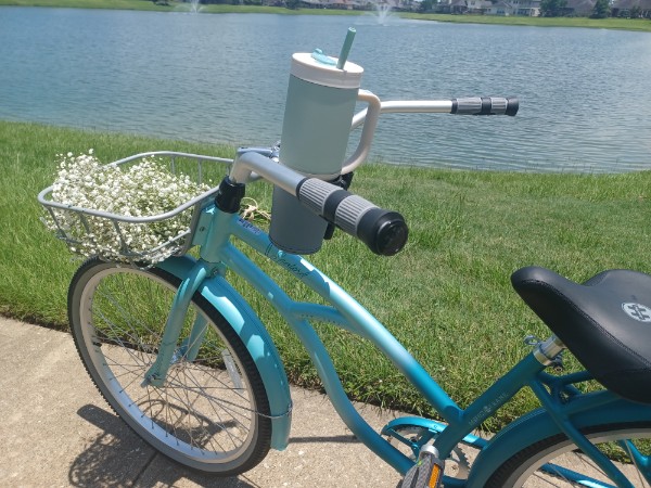 sanford women's beach cruiser bike, 26-in by a lake with white flowers in the front basket and a large water bottle.