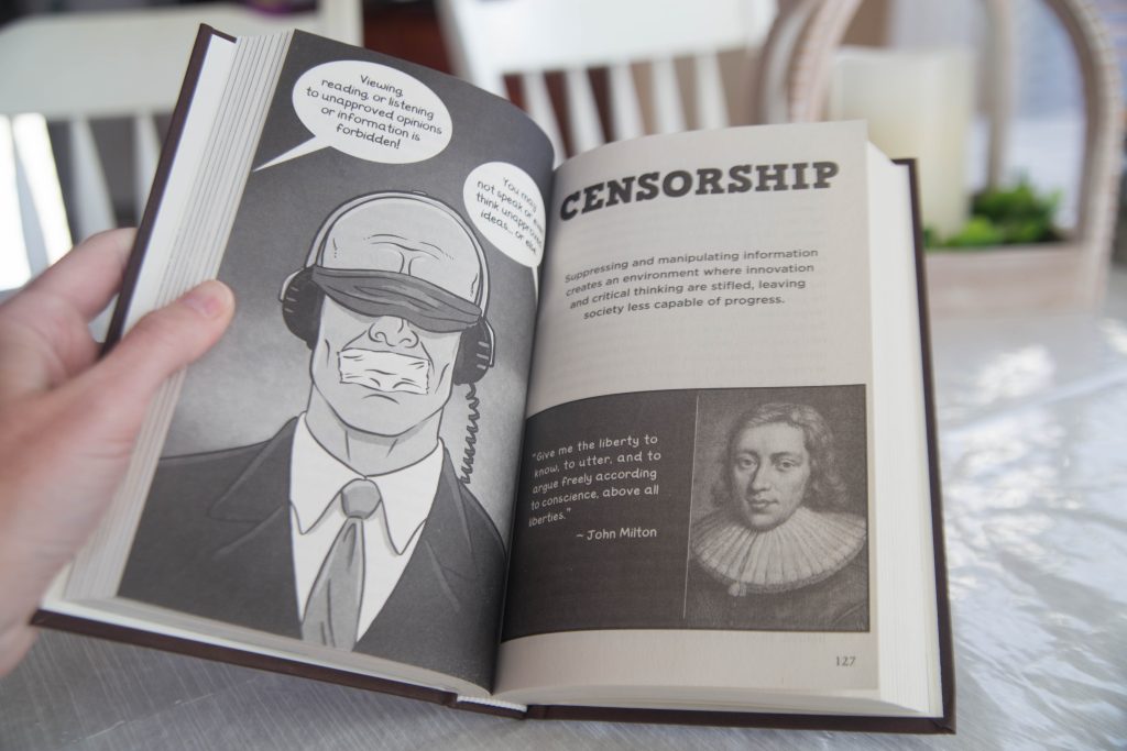 A hand holding an open book titled The Tuttle Twins Guide to the World's Worst Ideas by Connor Boyack 