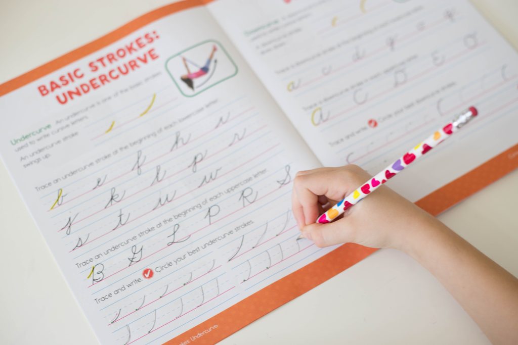 Homeschool child holding pencil and writing in a handwriting workbook