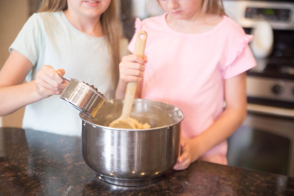 Two girls adding ingredients to a bowl baking chocolate chip cookies.